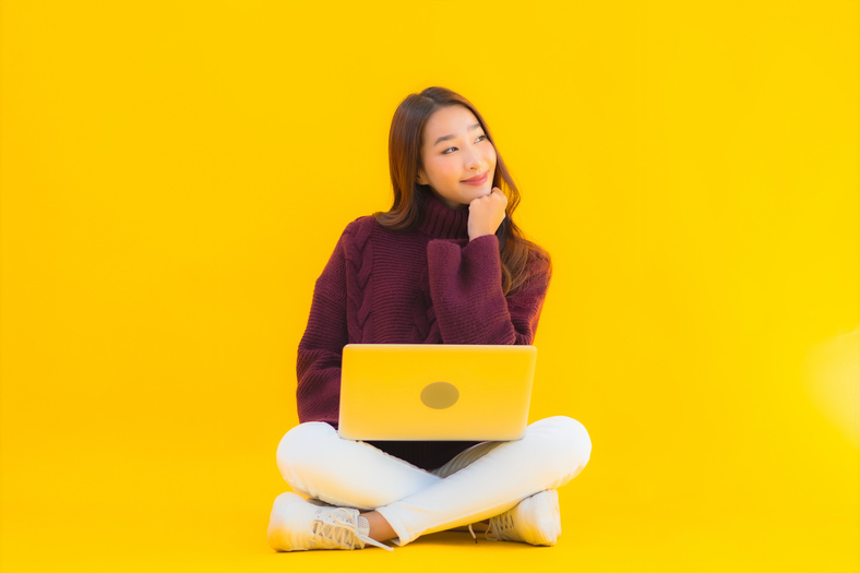Smiling Woman with Laptop Sitting on Yellow Background